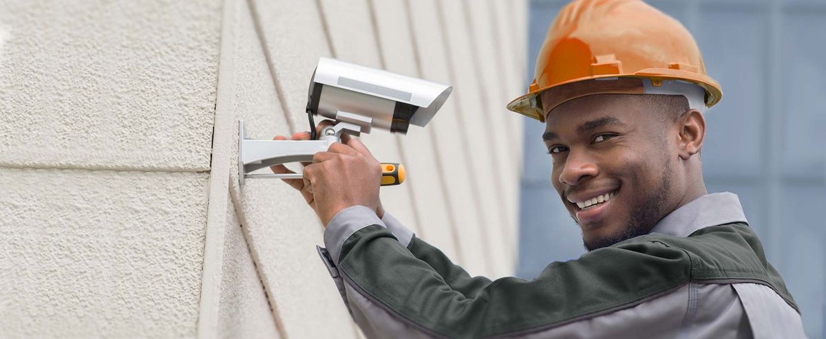 Technician in a hard hat installing a security camera on a commercial building in Edmonton