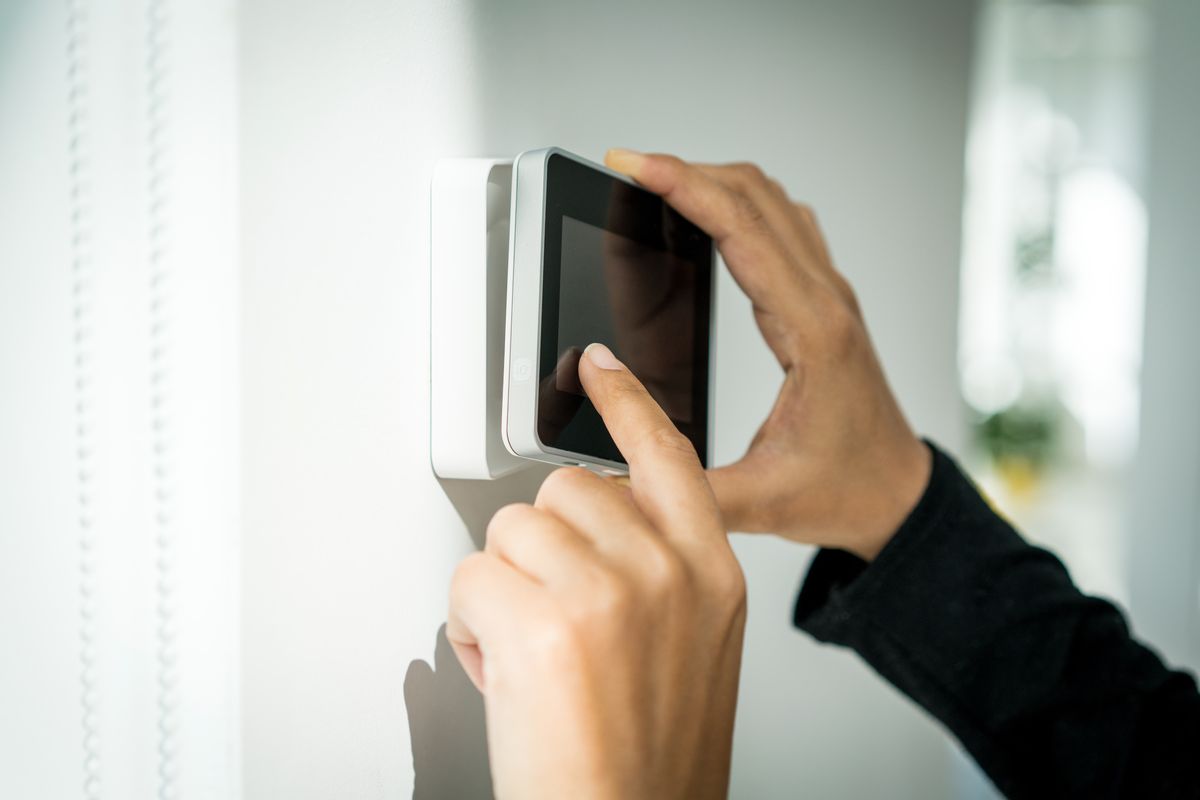 Hands mounting a touchscreen security alarm panel on a wall